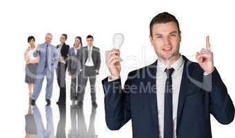 Composite image of businessman holding light bulb and pointing