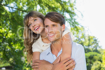 Man giving his pretty girlfriend a piggy back in the park smilin