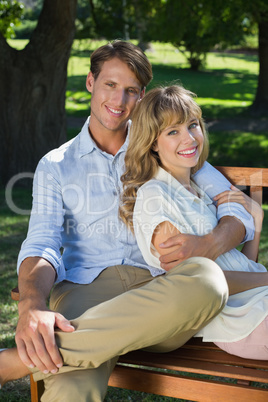 Affectionate couple relaxing on park bench together smiling at c