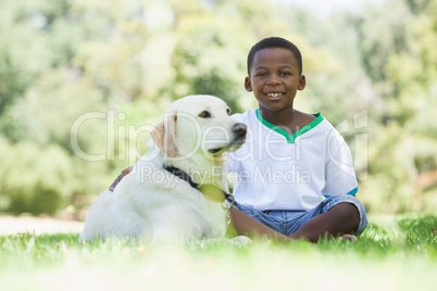 Little boy sitting with his pet labrador in the park