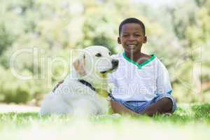 Little boy sitting with his pet labrador in the park