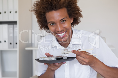 Casual smiling businessman eating sushi at his desk