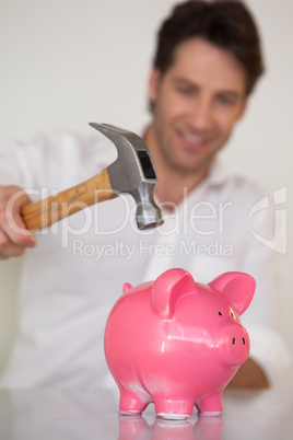 Casual businessman breaking piggy bank with hammer