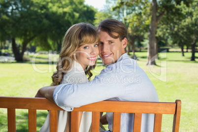 Couple relaxing on park bench together smiling at camera