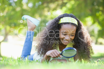 Young girl looking at grass through magnifying glass in the park