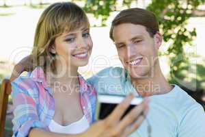 Cute couple sitting on bench in the park taking a selfie