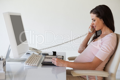 Casual pregnant businesswoman talking on phone at her desk