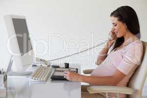 Casual pregnant businesswoman talking on phone at her desk