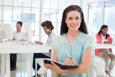 Attractive businesswoman writing in notebook and smiling to came