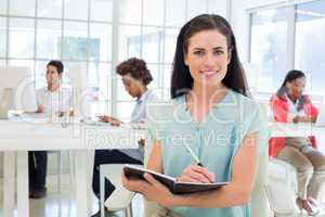 Attractive businesswoman writing in notebook and smiling to came