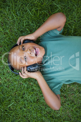 Little boy lying on grass listening to music smiling at camera