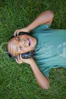 Little boy lying on grass listening to music smiling at camera