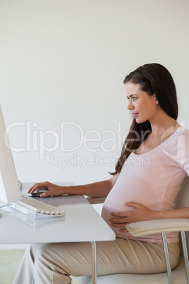 Casual pregnant businesswoman smiling at computer at her desk