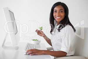 Casual pretty businesswoman eating a salad at her desk