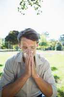 Stylish man blowing his nose in the park