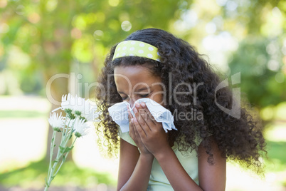 Young girl sitting by flower and blowing her nose in the park