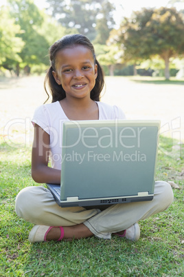 Little girl sitting on grass using laptop smiling at camera