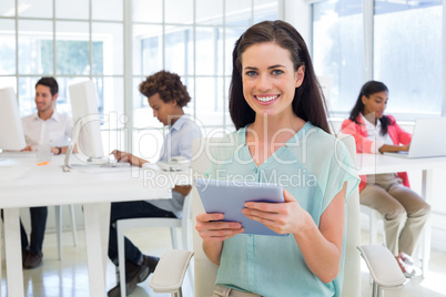 Businesswoman on tablet pc smiling at camera with colleagues beh