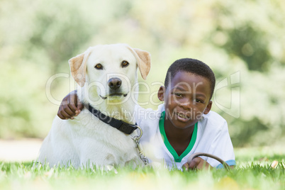 Little boy lying with his pet labrador in the park