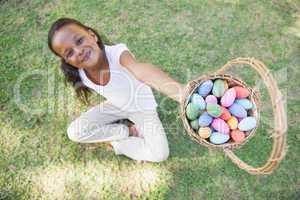 Little girl sitting on grass showing basket of easter eggs to ca