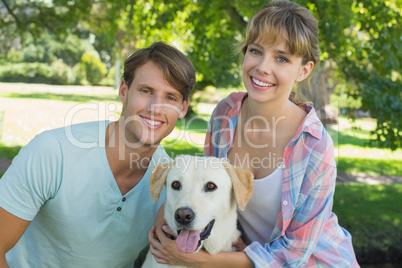 Happy couple sitting with their labrador in the park smiling at