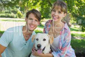 Happy couple sitting with their labrador in the park smiling at