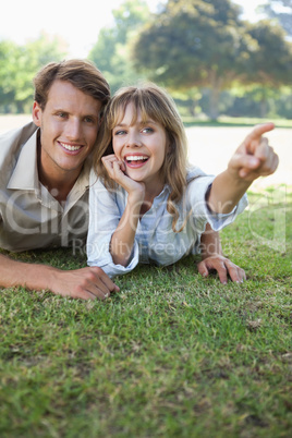 Carefree couple lying in the park with woman pointing
