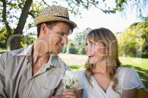 Smiling man offering his girlfriend a white flower in the park