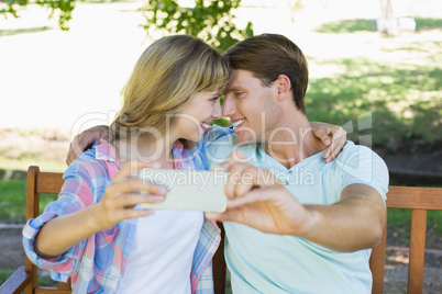 Smiling couple sitting on bench in the park taking a selfie