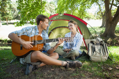 Cute man serenading his girlfriend on camping trip