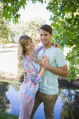 Loving young couple standing together in the park smiling at cam