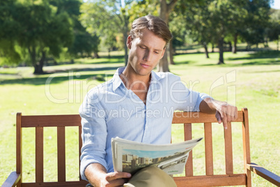 Handsome man sitting on park bench reading newspaper