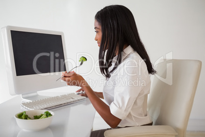 Casual pretty businesswoman eating a salad at her desk