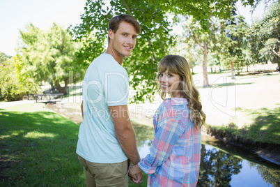 Cute couple walking hand in hand in the park smiling at camera