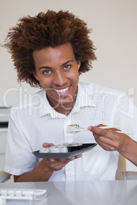Casual smiling businessman eating sushi at his desk