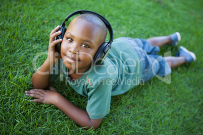 Little boy lying on grass listening to music smiling at camera