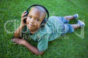 Little boy lying on grass listening to music smiling at camera