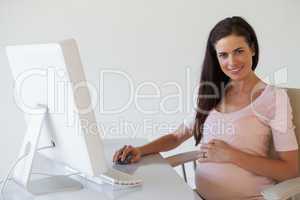 Casual pregnant businesswoman smiling at camera at her desk