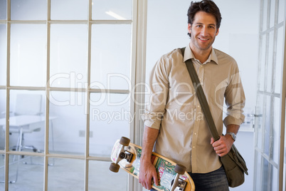 Casual businessman standing with his skateboard smiling at camer