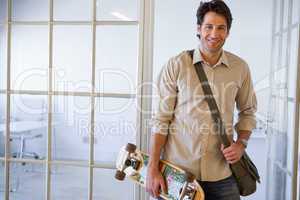 Casual businessman standing with his skateboard smiling at camer