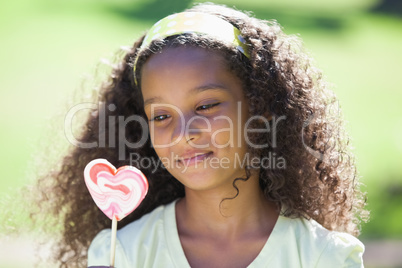 Young girl holding a heart lollipop in the park