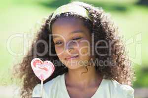 Young girl holding a heart lollipop in the park