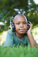 Little boy lying on grass listening to music smiling at camera