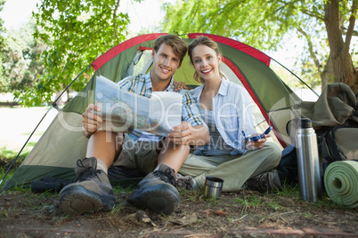 Cute couple sitting by tent reading a map smiling at camera