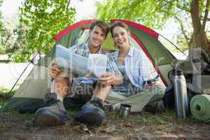 Cute couple sitting by tent reading a map smiling at camera