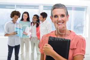 Businesswoman holds planner and smiles at camera while colleague