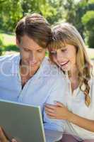 Cute couple sitting on park bench together looking at laptop