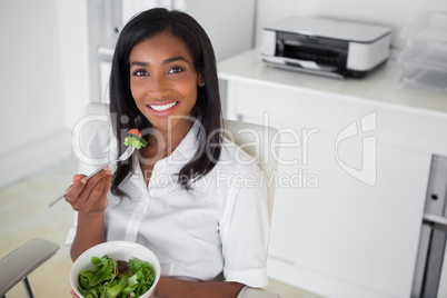 Casual pretty businesswoman eating a salad at her desk