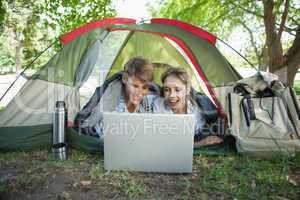 Cute couple lying in their tent using laptop