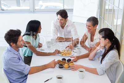 Business people chat while eating muffins and drinking coffee